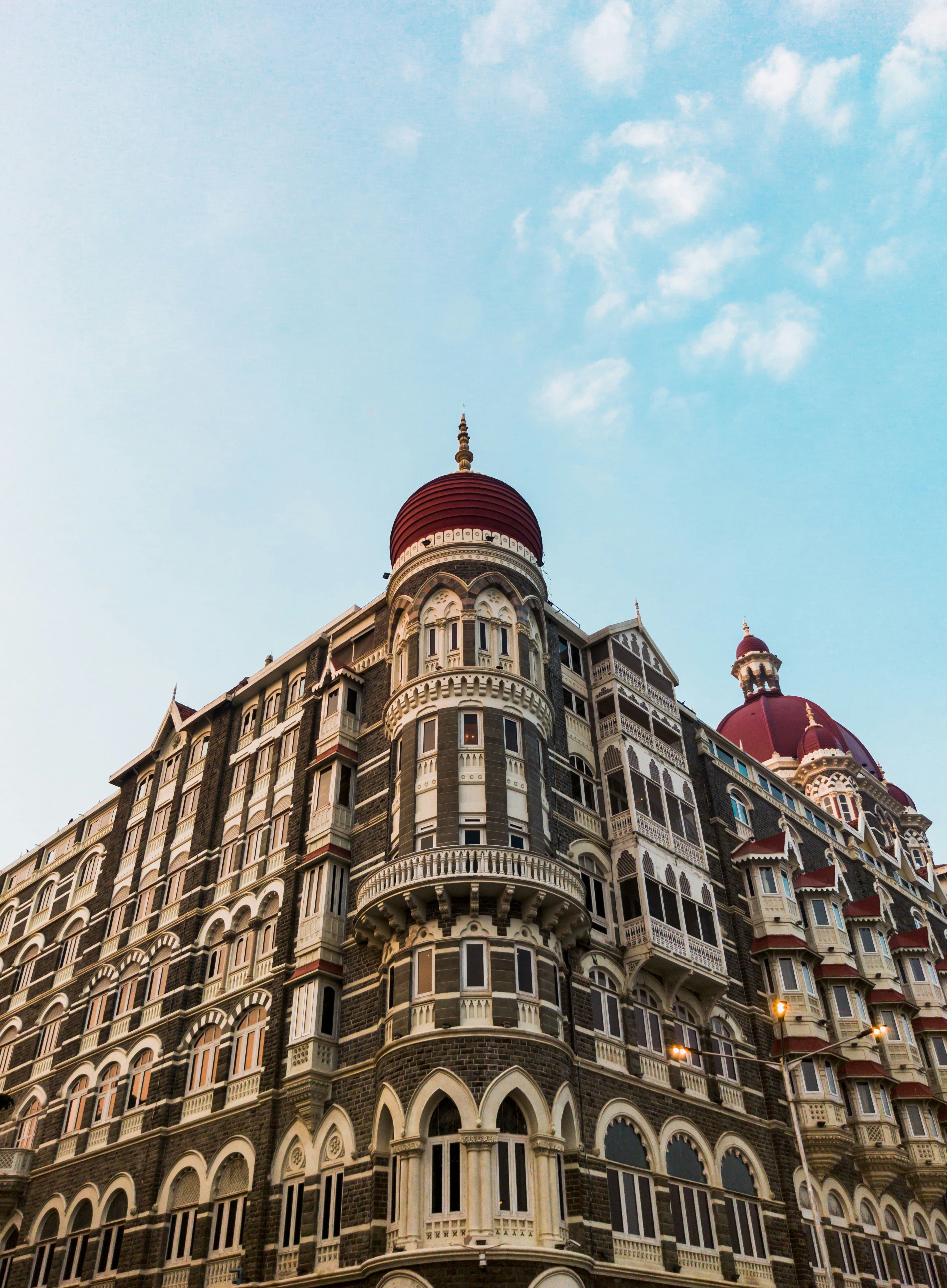 The red domes and ornate facade of the Taj Mahal Palace beneath a blue sky with white clouds in Mumbai