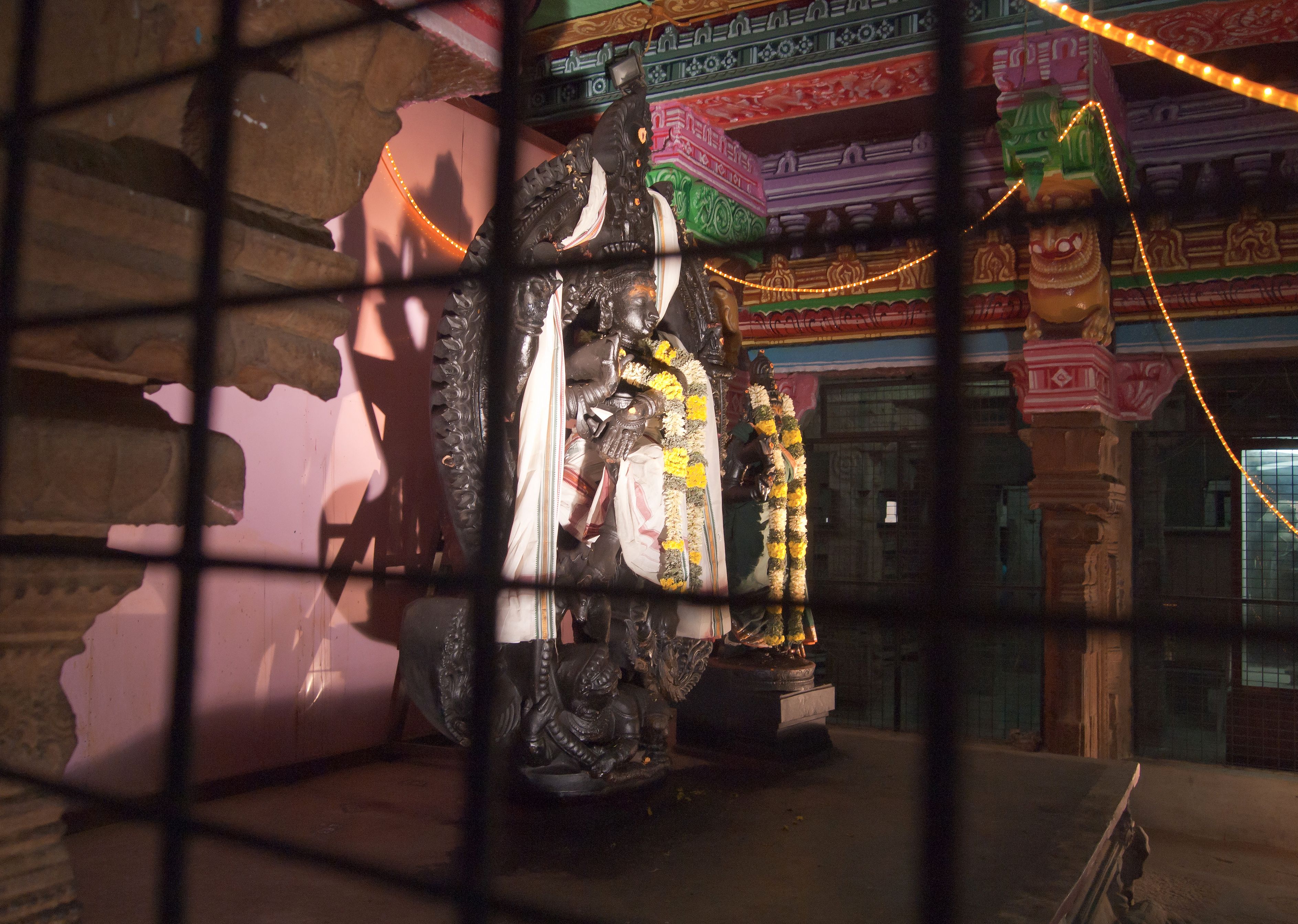 Light falling on painted columns and a sculpted figure inside the Meenakshi temple complex in Madurai