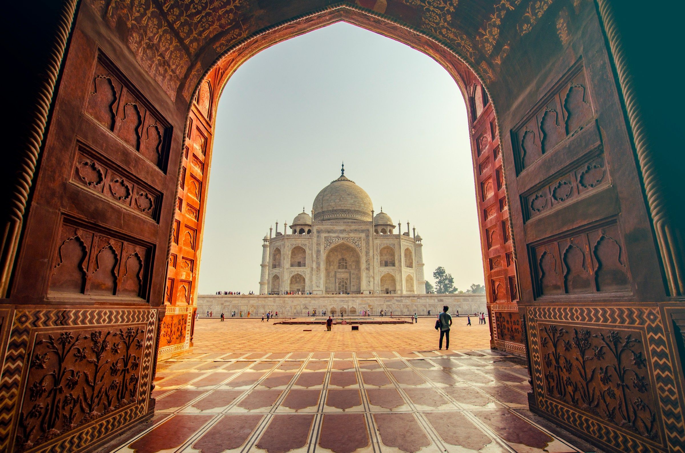 The Taj Mahal framed by carved sandstone arches in warm morning light