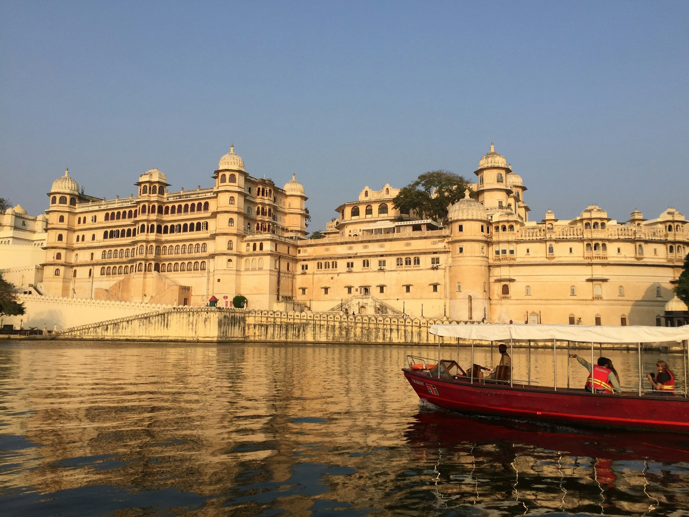A covered boat passing Udaipur City Palace in golden evening light