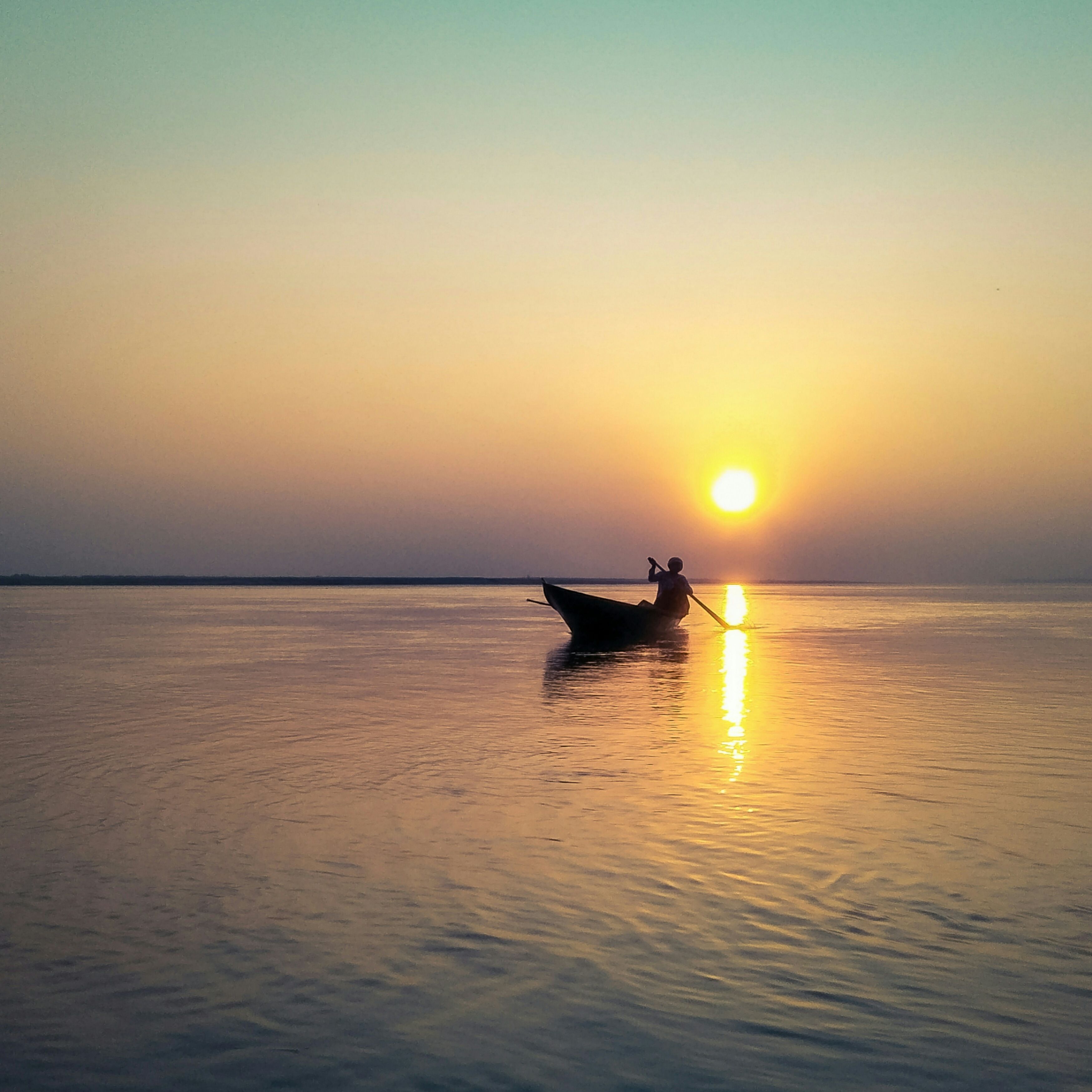 A wooden boat silhouetted against a golden sunset on the Brahmaputra River in Assam
