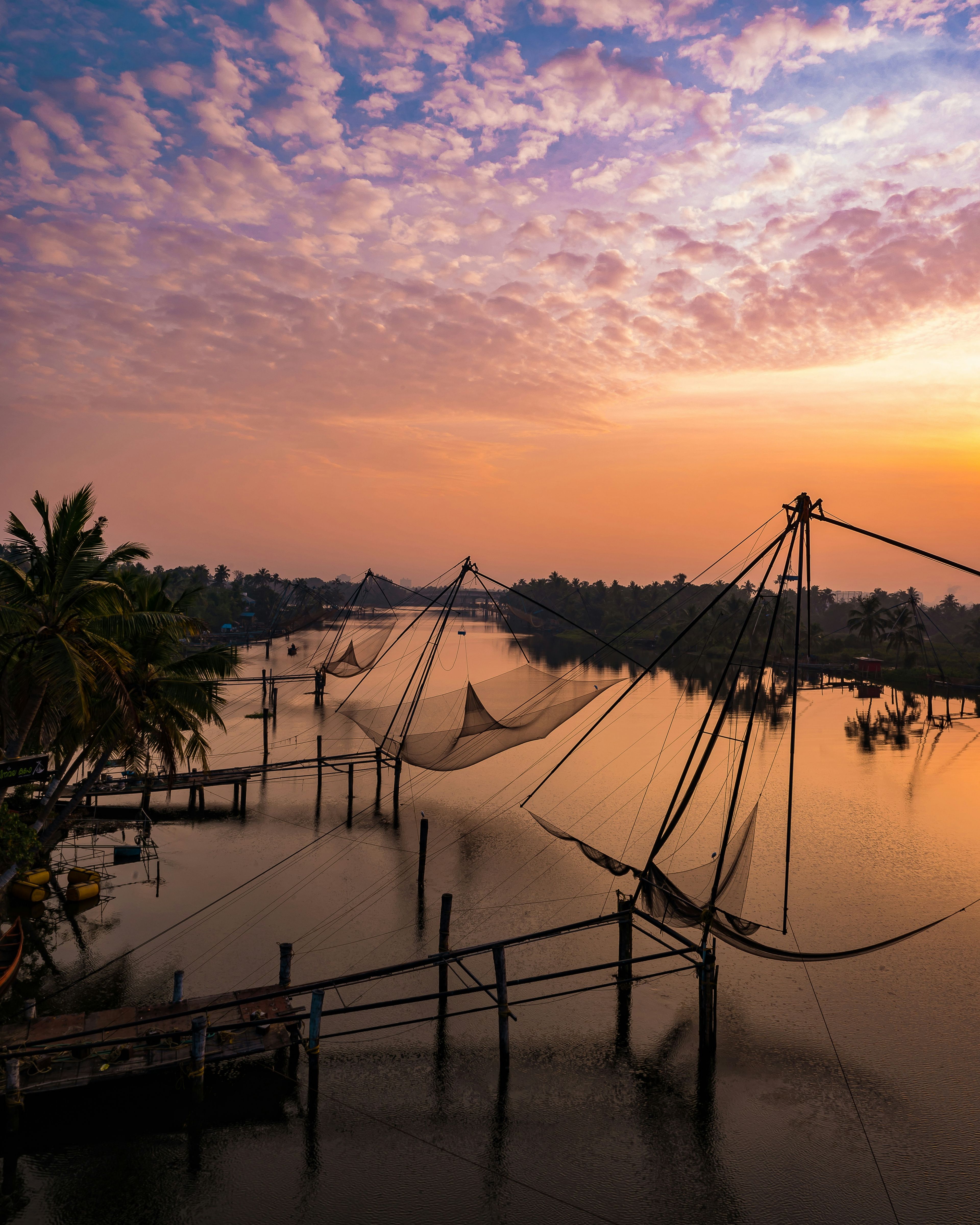 Chinese fishing nets reflected in still water beneath rose-coloured sunset clouds in Kochi