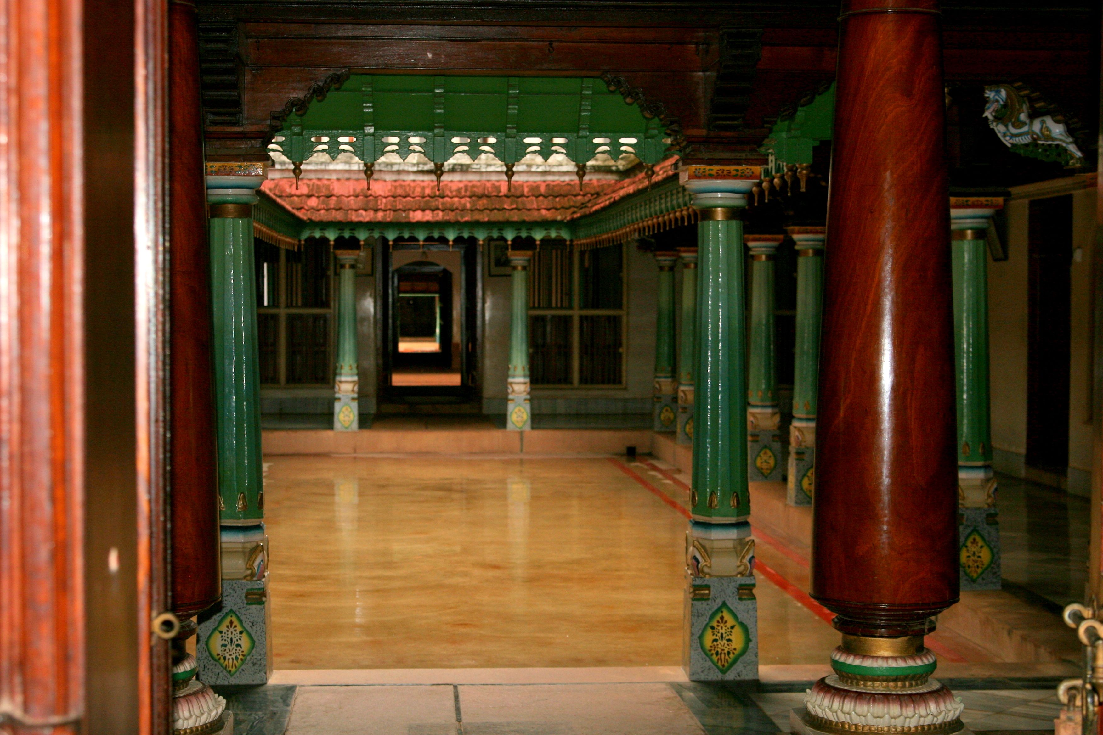 Polished wooden columns and painted stone pillars framing a quiet courtyard in a traditional Chettinad house