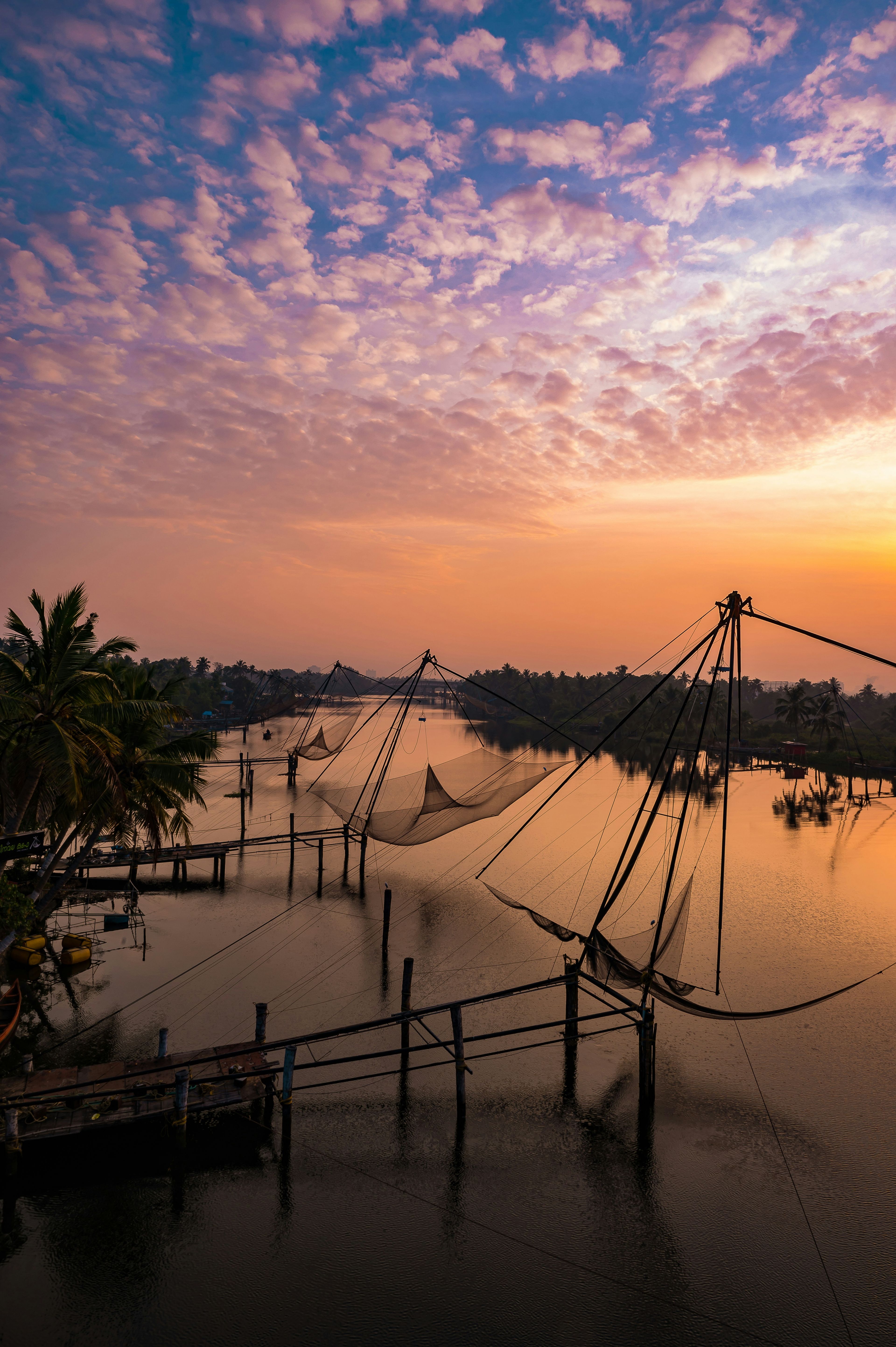 Chinese fishing nets reflected in still water beneath rose-coloured sunset clouds in Kochi