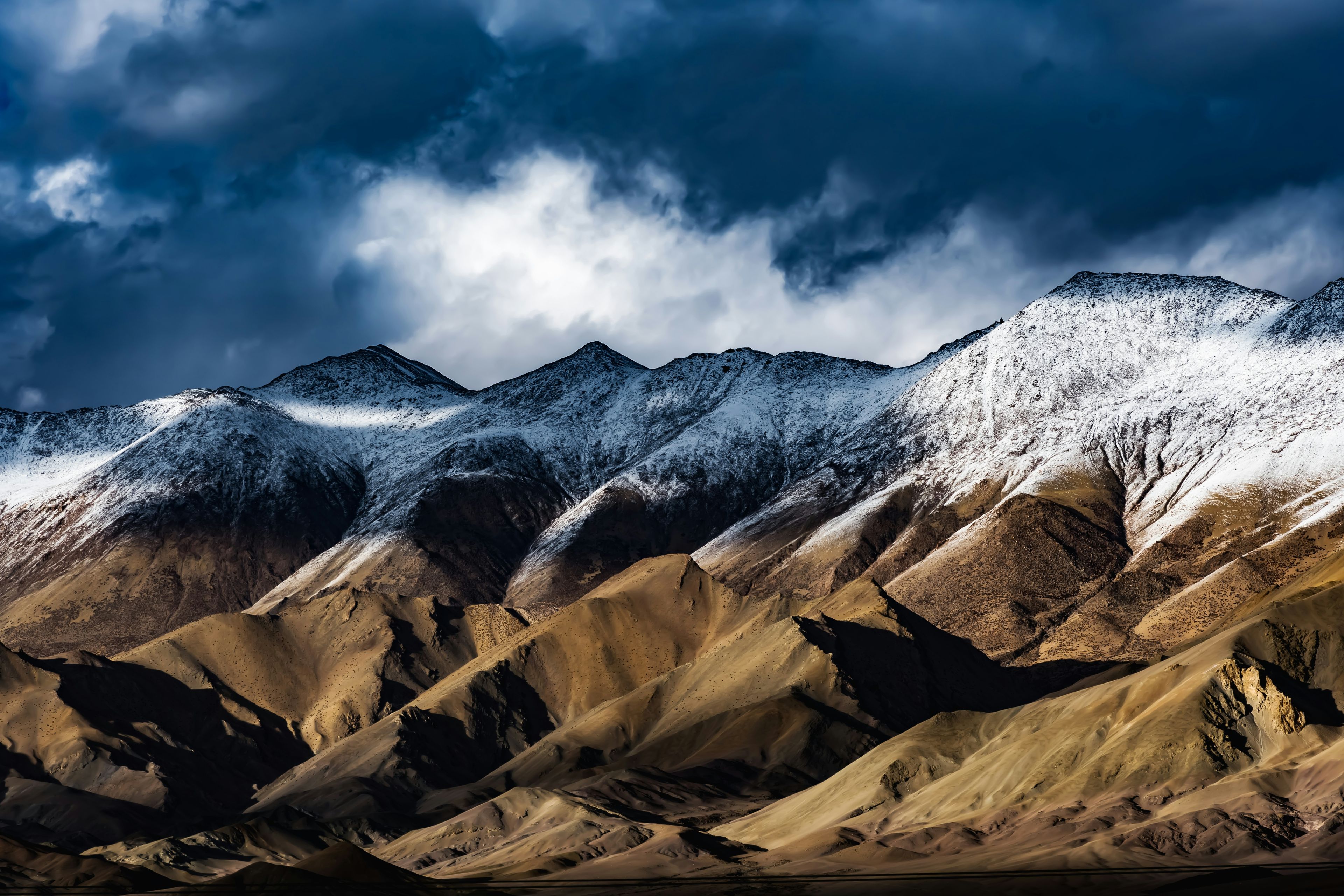 Snow-dusted mountain ridges beneath dramatic clouds near Hanle in Ladakh