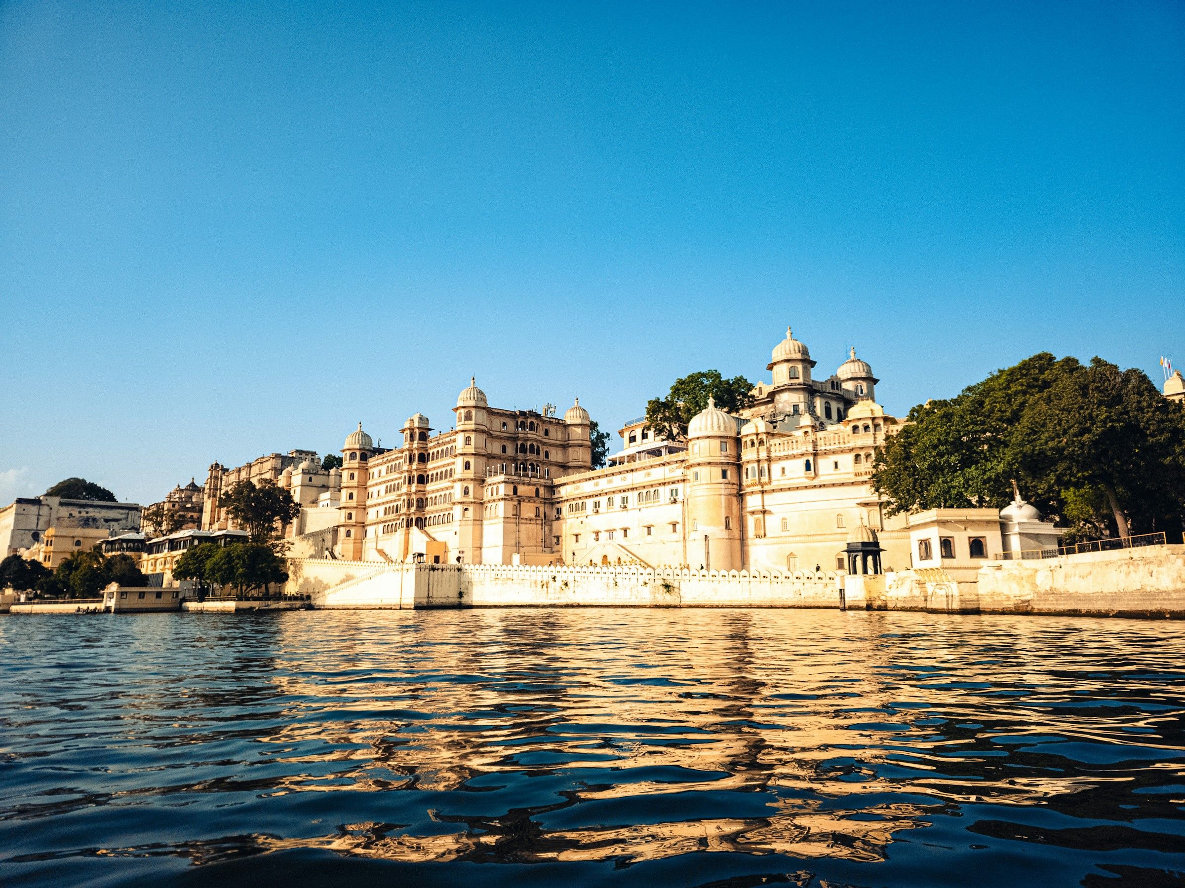 Sunlit Udaipur City Palace reflected in the blue waters of Lake Pichola