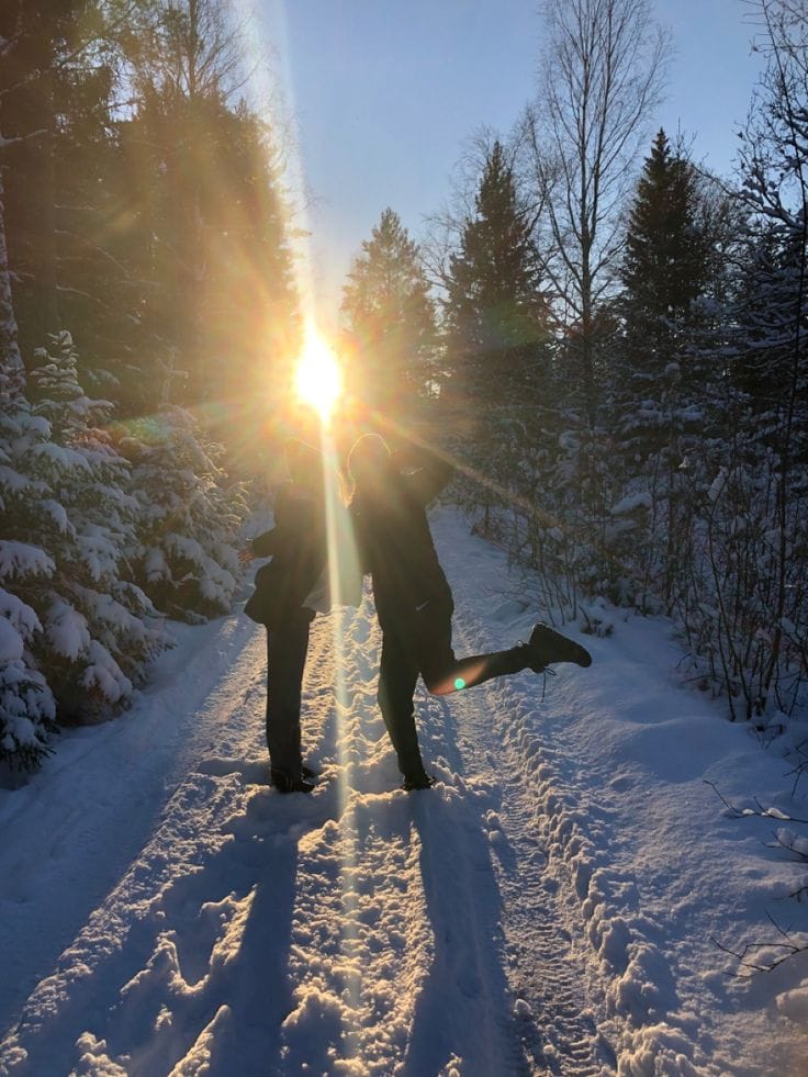 A couple standing on a snowy path in low sunlight