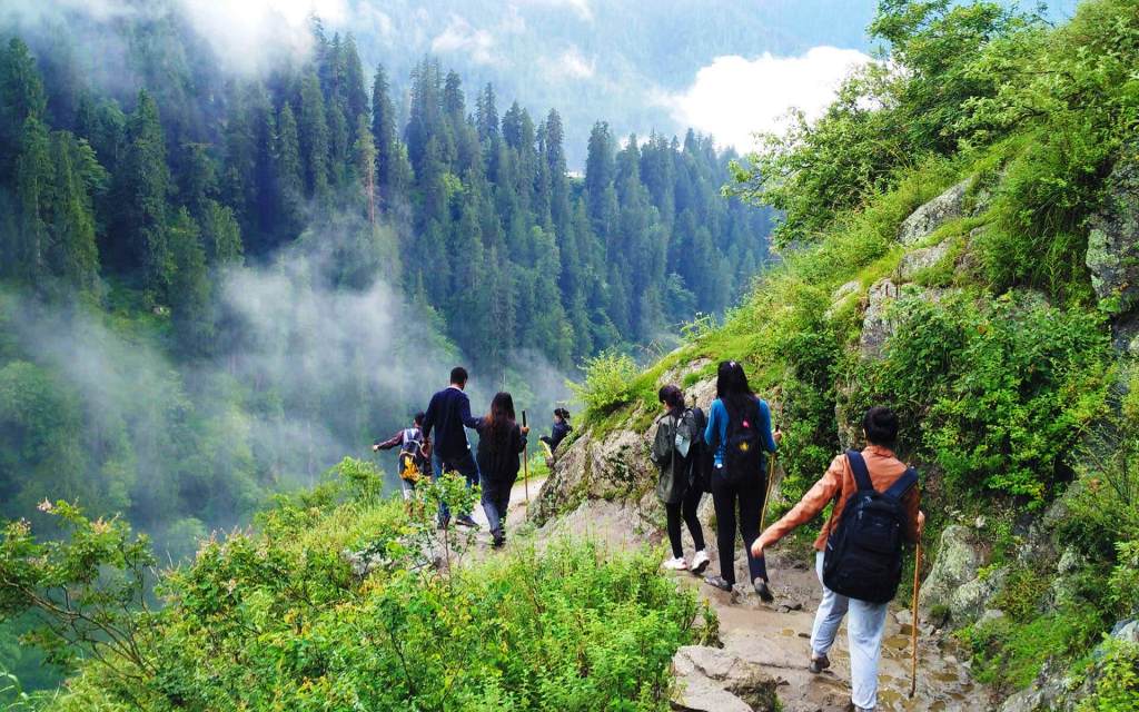 Hikers following a grassy trail through a green mountain valley