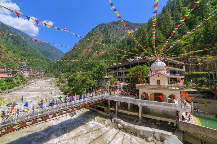 A small riverside shrine beneath prayer flags and green mountains