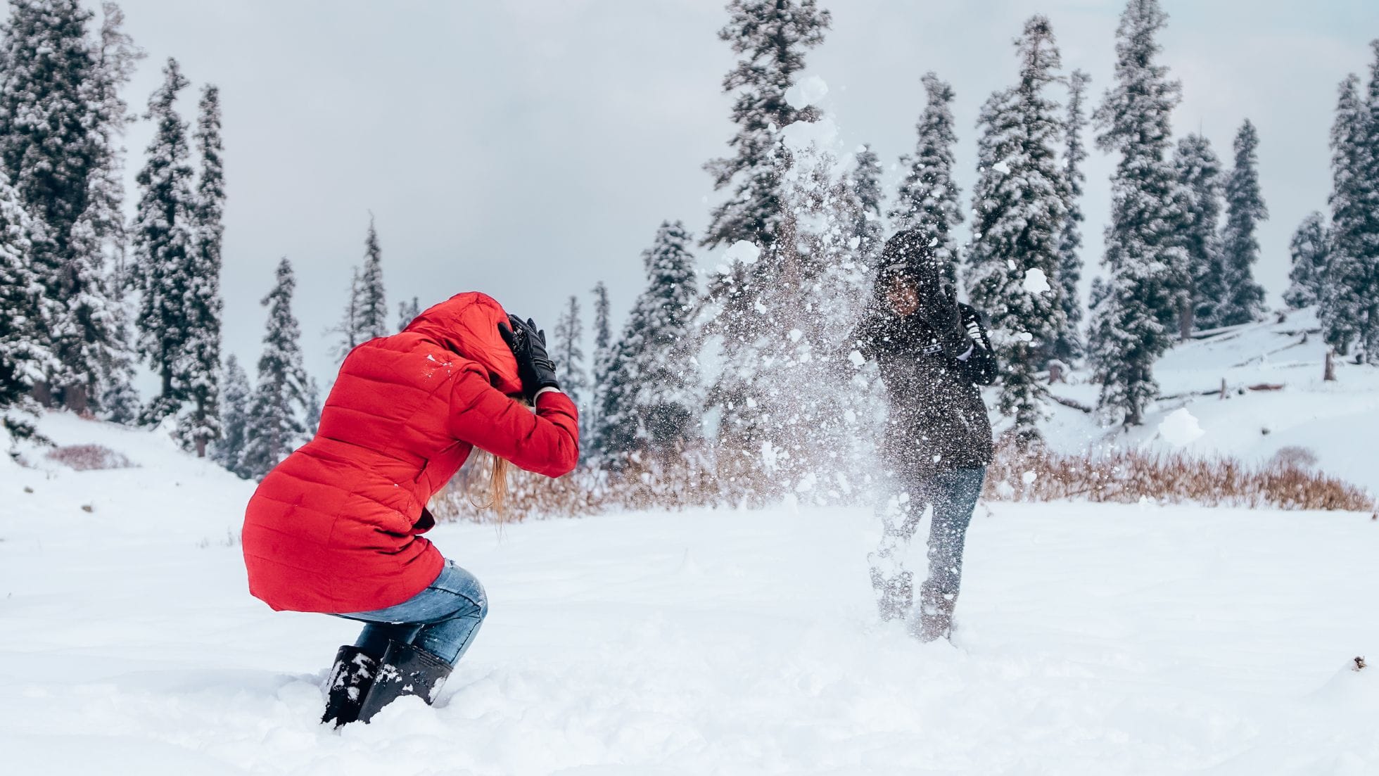 A person photographing another playing in the snow