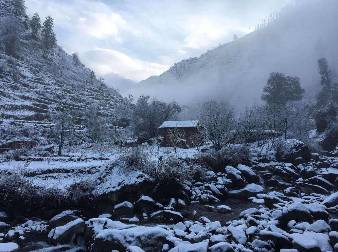A snowy mountain stream and houses beneath misty hills