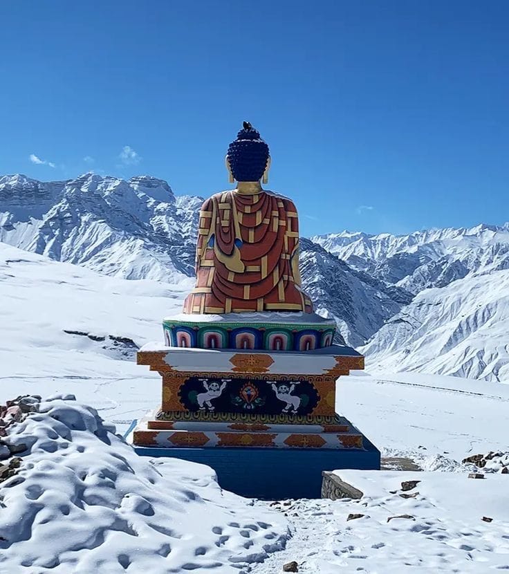 A seated Buddha statue on a snowy mountain terrace