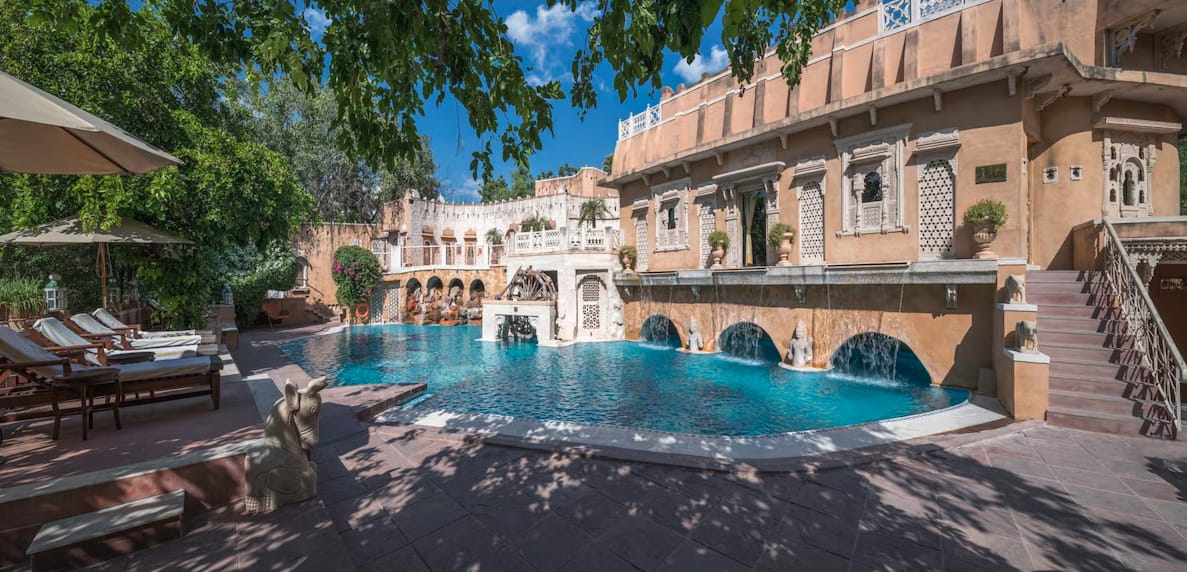 A swimming pool beneath arched galleries and trees