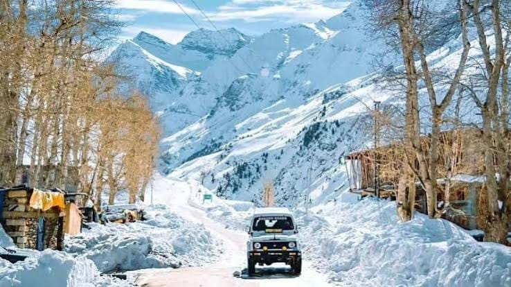 A jeep on a snowy road below high mountain peaks