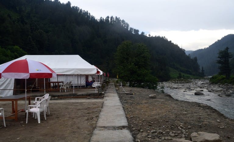 A riverside camp terrace with seating and a sun umbrella
