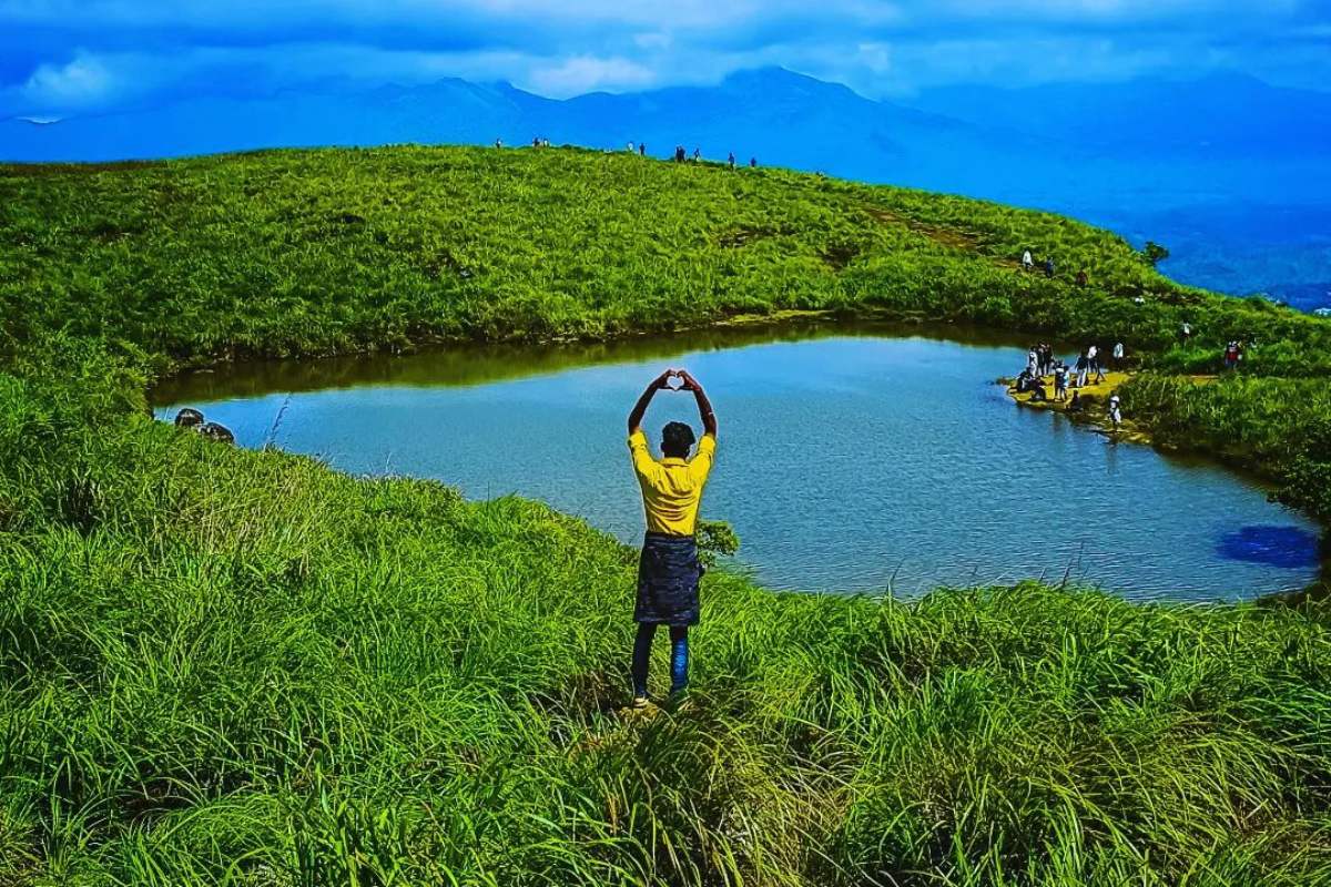 A visitor standing beside a small hilltop lake