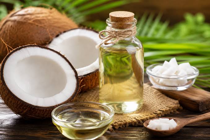 Coconut halves beside a bottle and bowls of coconut oil