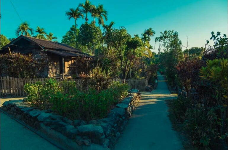 A paved village path beside gardens and a traditional house
