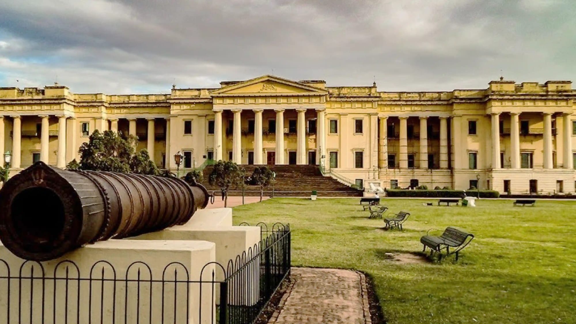 A historic columned palace with a cannon in the foreground