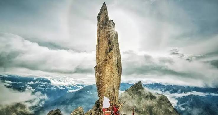 A tall standing rock above cloud-covered mountains