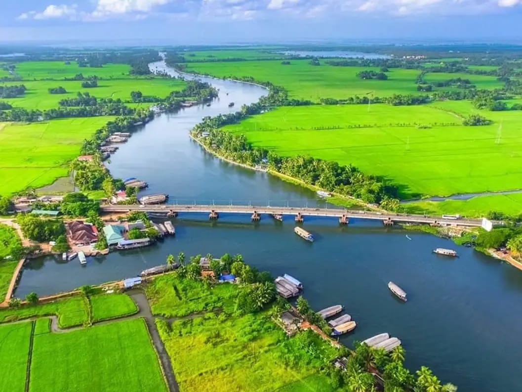 A river winding through rice fields with boats near a bridge
