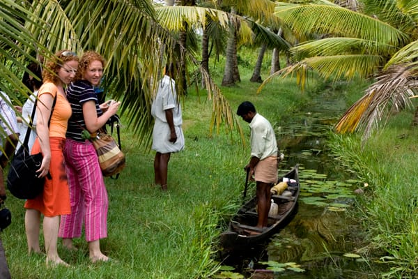 Visitors watching a boatman beside a palm-lined canal