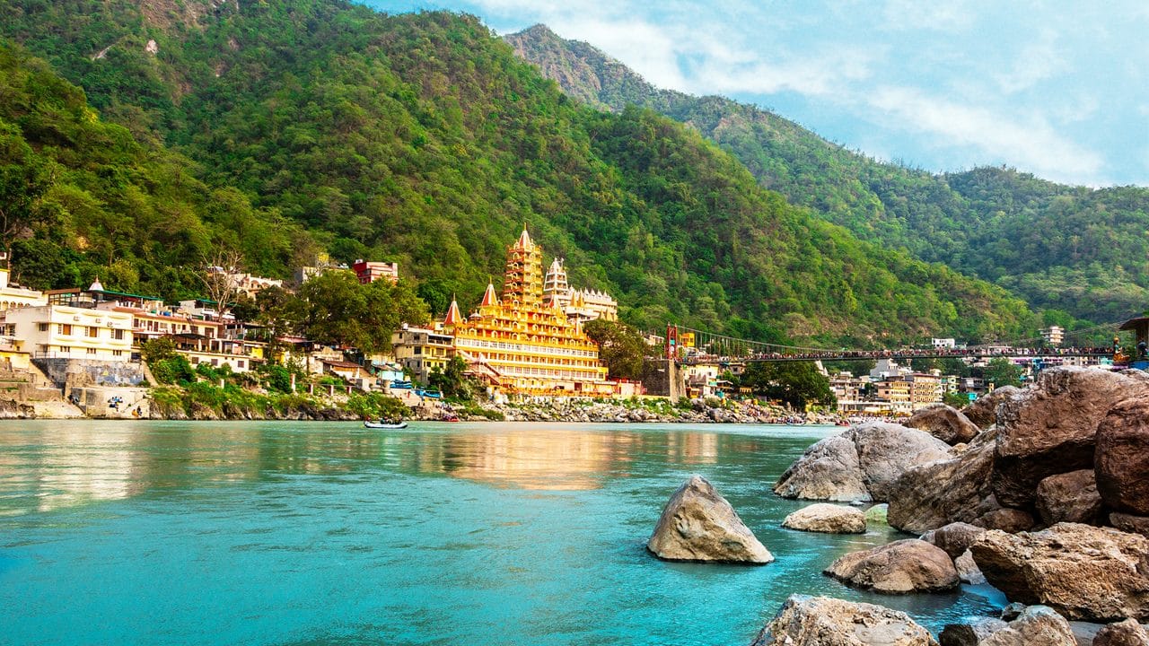 A riverside temple beside turquoise water and wooded hills