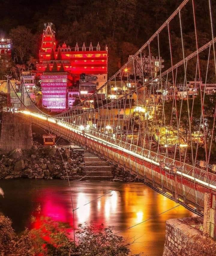A suspension bridge and riverside buildings illuminated at night