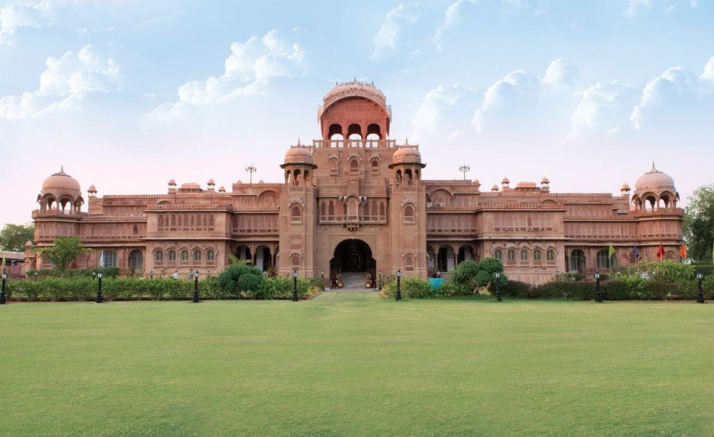 A red sandstone palace facade beyond a green lawn