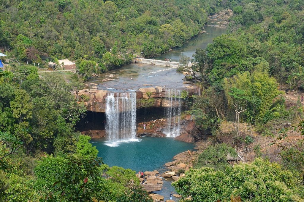A broad waterfall flowing into a pool surrounded by green hills