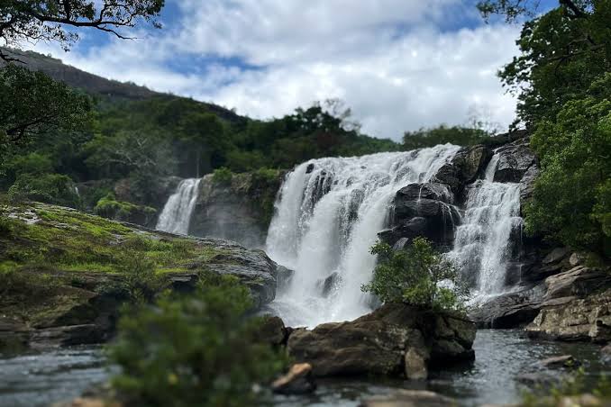 A broad waterfall flowing over rocks in a wooded valley