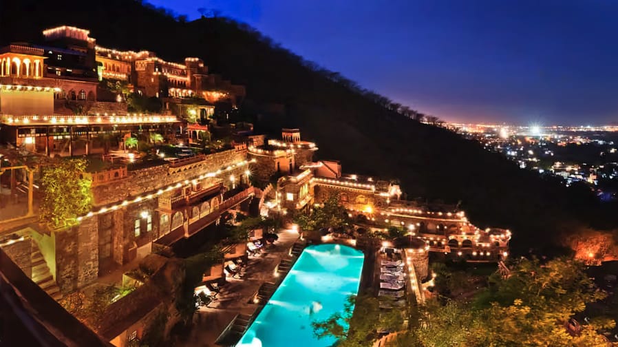 An illuminated hillside fort hotel with a swimming pool