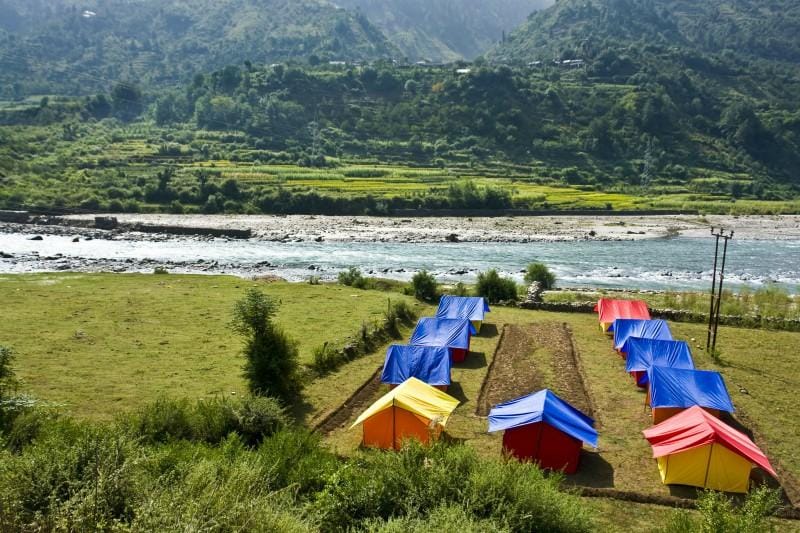 Outdoor chairs on a grassy campsite beside a mountain river