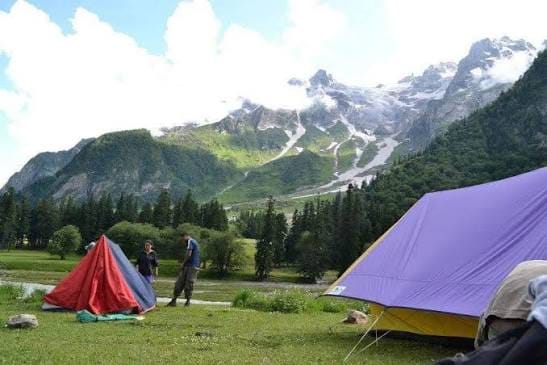Tents pitched below a snow-streaked mountain ridge