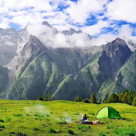 Small tents on a green meadow beneath steep mountain peaks