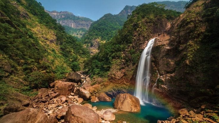 A waterfall plunging into a green pool in a wooded valley