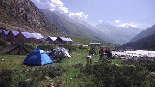 A riverside campsite with tents beneath steep mountains