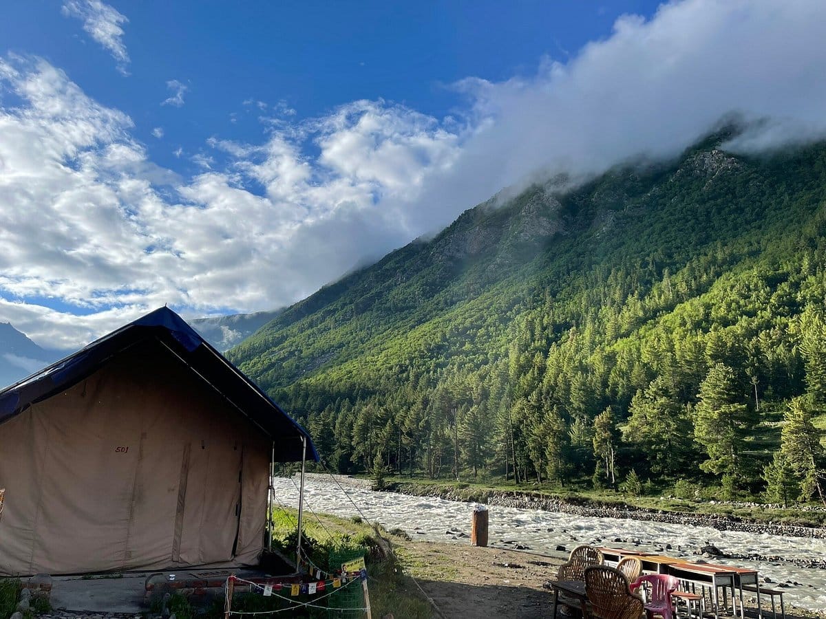 A canvas tent beside a river beneath forested slopes