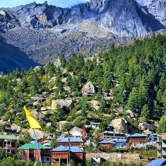 Village buildings among tall conifers beneath snowy peaks