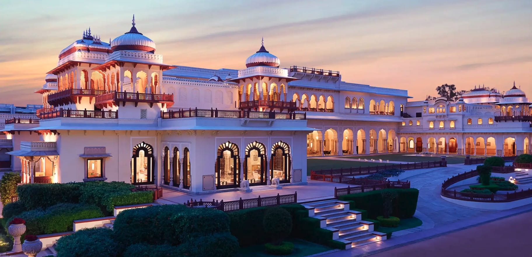 An illuminated heritage hotel with domed pavilions at dusk