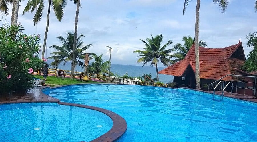 A swimming pool bordered by palm trees and tiled-roof buildings