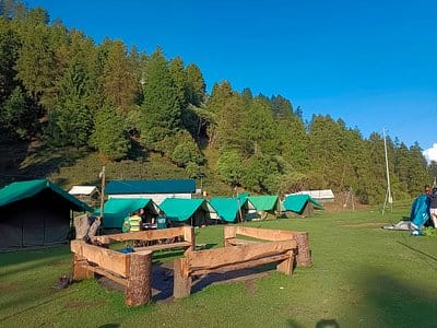 A green mountain campsite with tents and outdoor seating