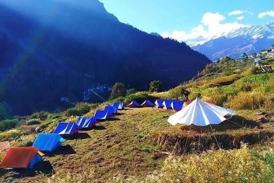 Colorful tents across a grassy slope below snow-capped mountains