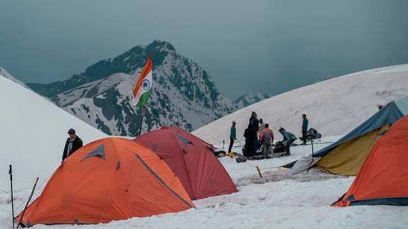 Orange tents pitched on snow beneath a mountain peak