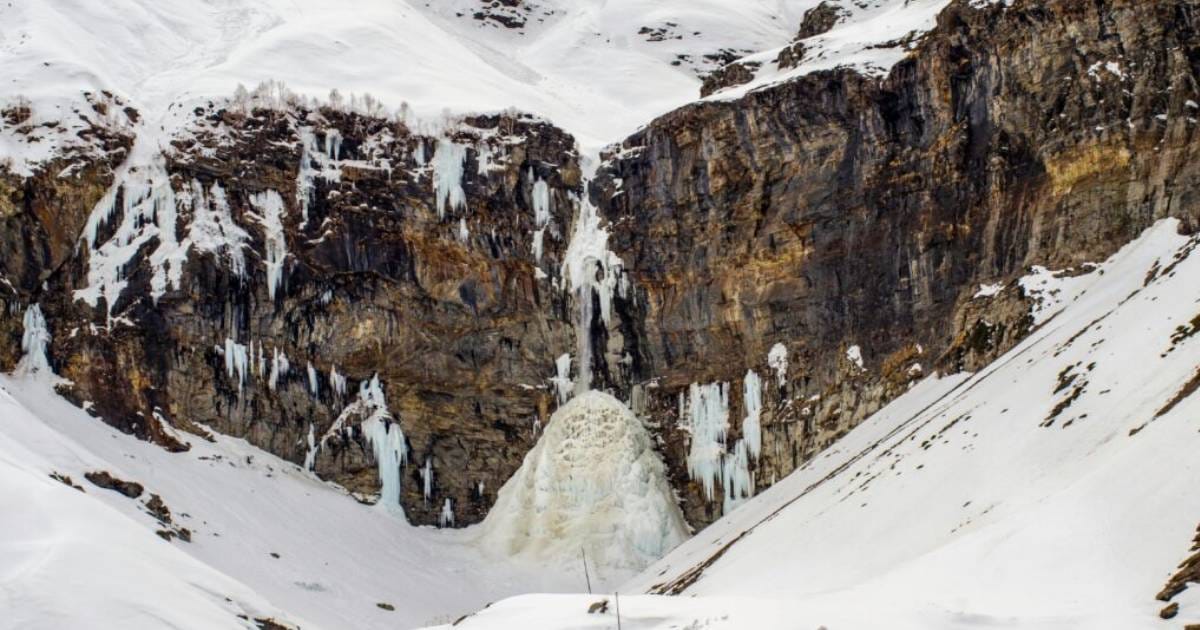 A partly frozen waterfall descending a snow-covered cliff