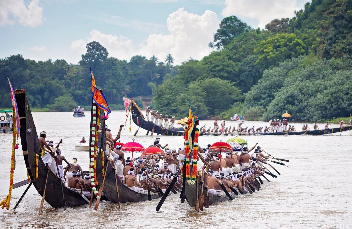 Crews rowing long boats on a river below wooded hills