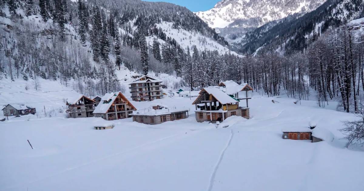 Cottages in a snowy valley below forested mountains