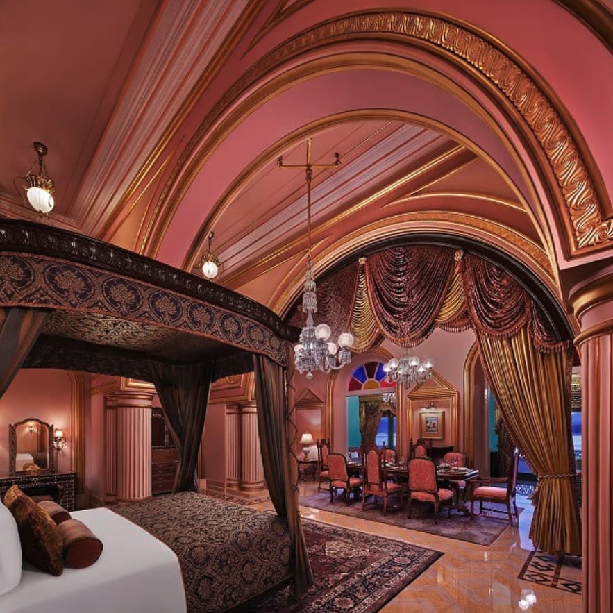 An ornate vaulted hotel suite with seating and a bed