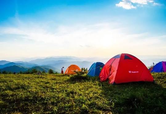 Bright tents pitched on a grassy ridge beneath blue skies