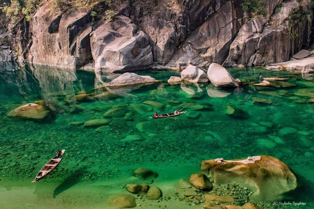 A small boat on clear green water beside large boulders